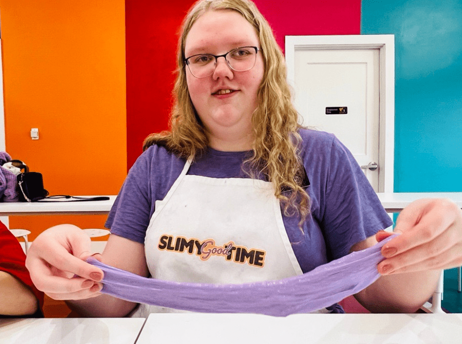 Amy smiles for the camera while she stretches out a piece of purple slime.