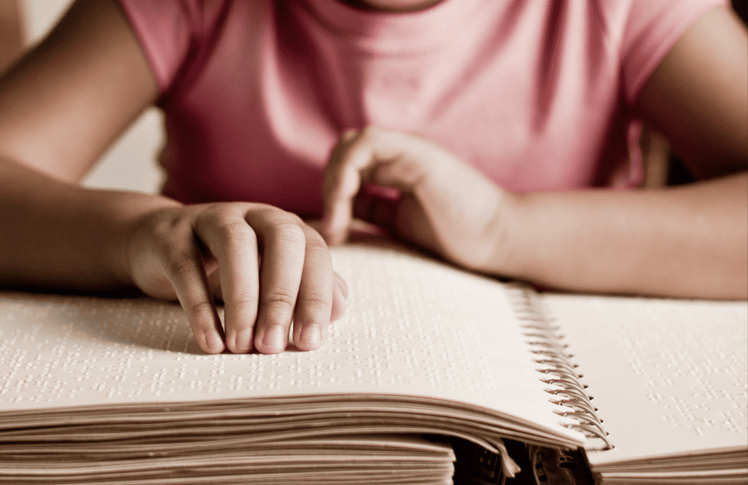 A little girl in a pink shirt is shown reading a braille book.