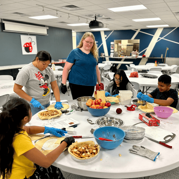 A female volunteer helps a group of students with making pies.