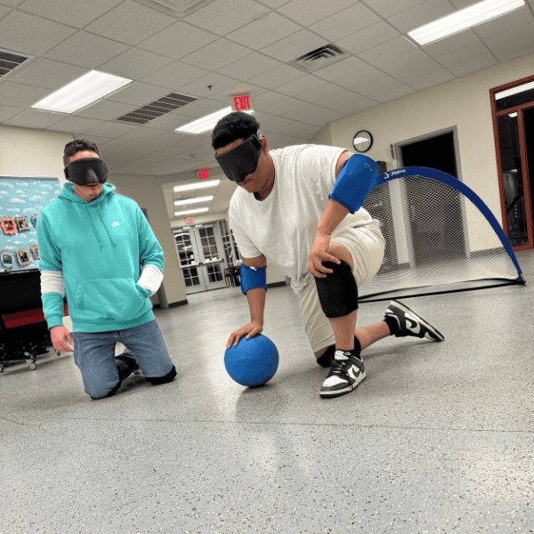 A male adult helps plays goalball with a kid.