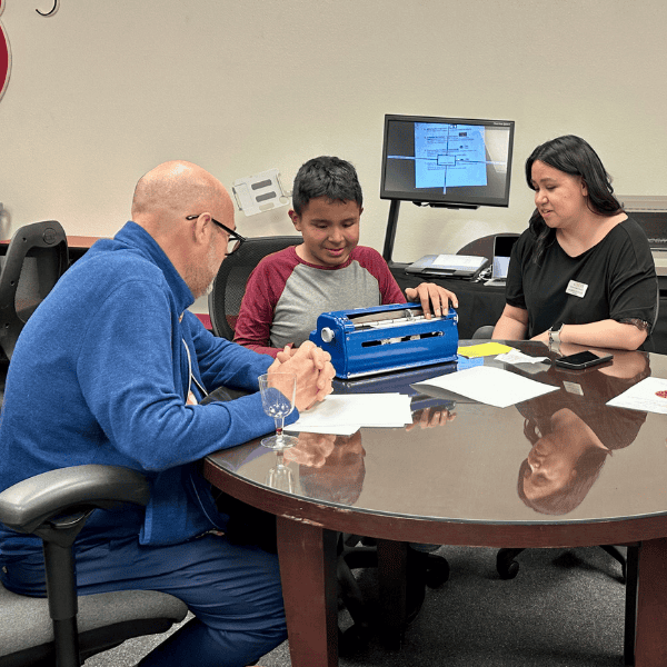 A man and a woman learn from a student how to use the braille machine.