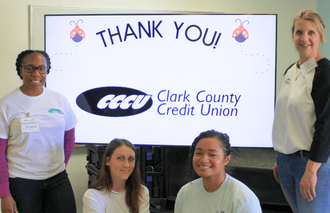 Volunteers from Clark County Credit Union pose in front of a 'Thank You!' banner displaying the Clark County Credit Union logo. The group wears matching white t-shirts, showing unity and team spirit at the Friendsgiving event.