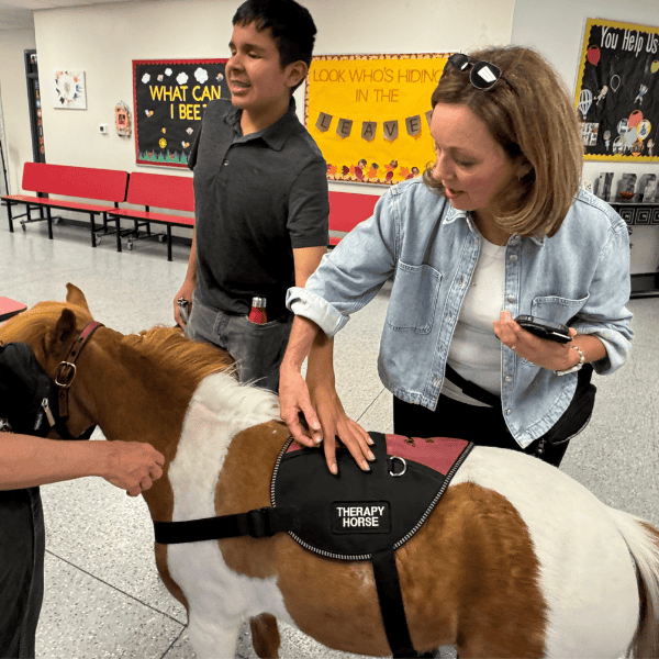A woman helps a young boy with visual impairments pet a tiny horse.